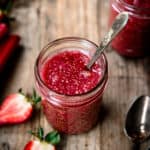 High side angle view of rhubarb chia compote in a glass jar with spoon on wooden table