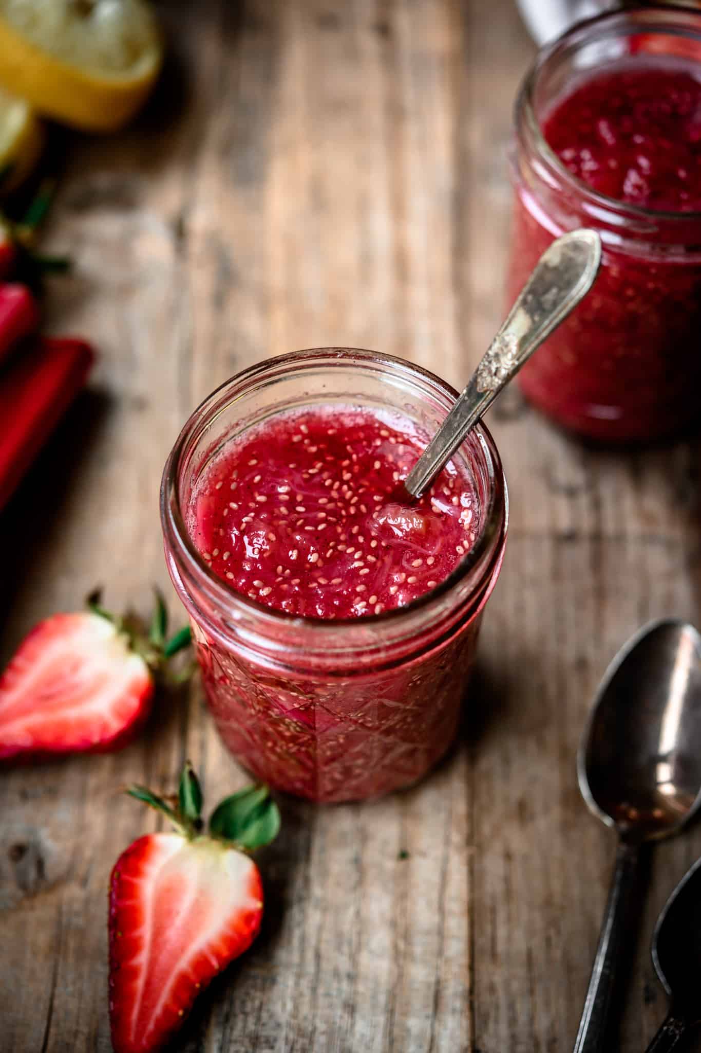 High side angle view of rhubarb chia compote in a glass jar with spoon on wooden table
