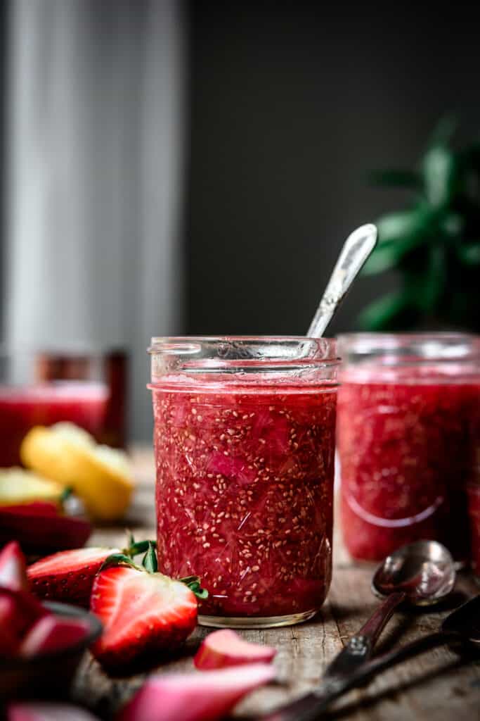 Side view of jar of rhubarb vanilla chia compote on a wood table, dark and moody photo