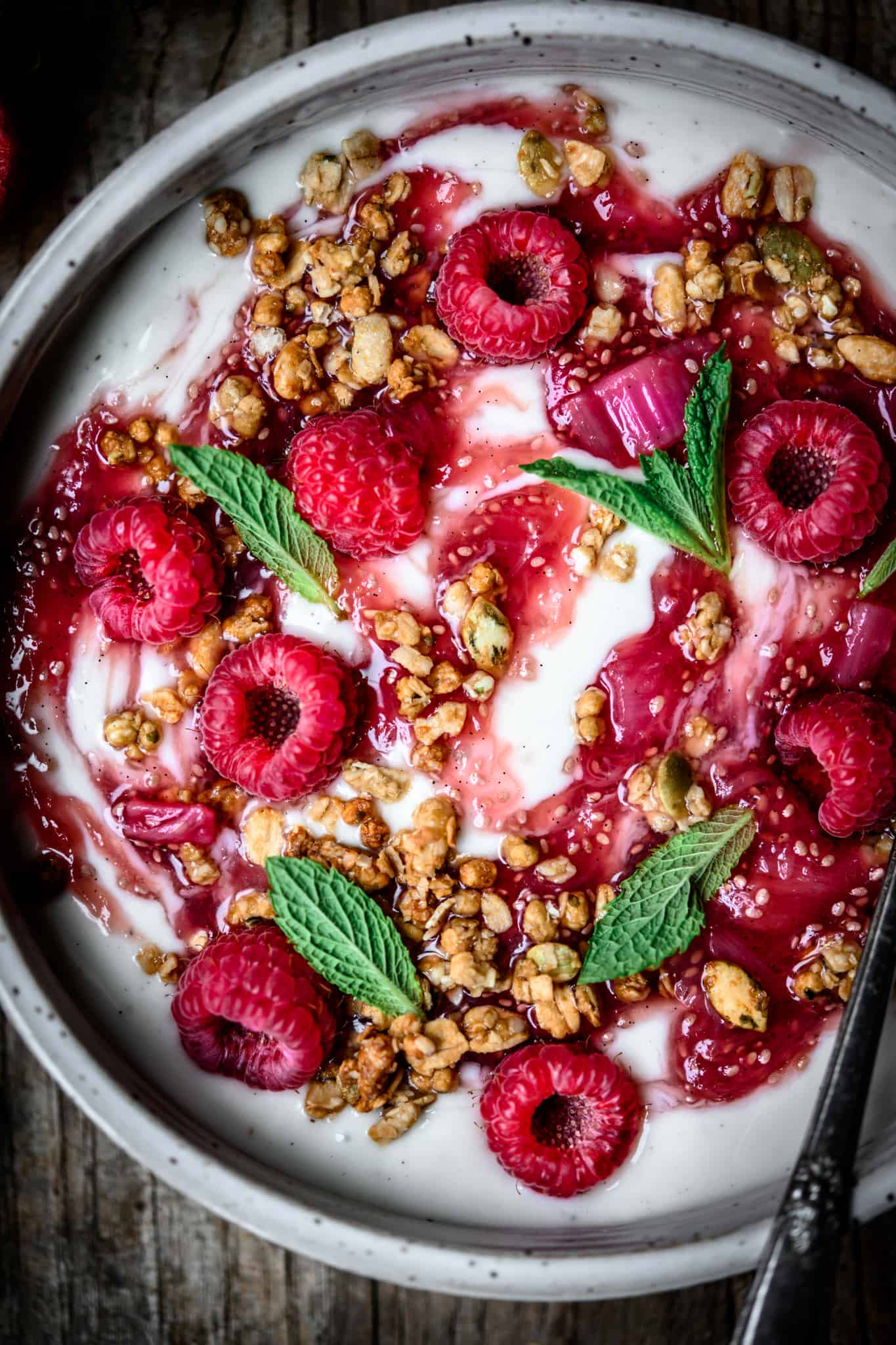 Close up overhead view of vanilla yogurt with rhubarb compote, granola, raspberries and mint