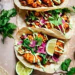 Close up Overhead view of 3 spicy black bean and cauliflower tacos with pickled red onion on light brown background