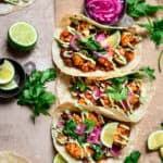 Overhead view of 3 spicy black bean and cauliflower tacos with pickled red onion on light brown background