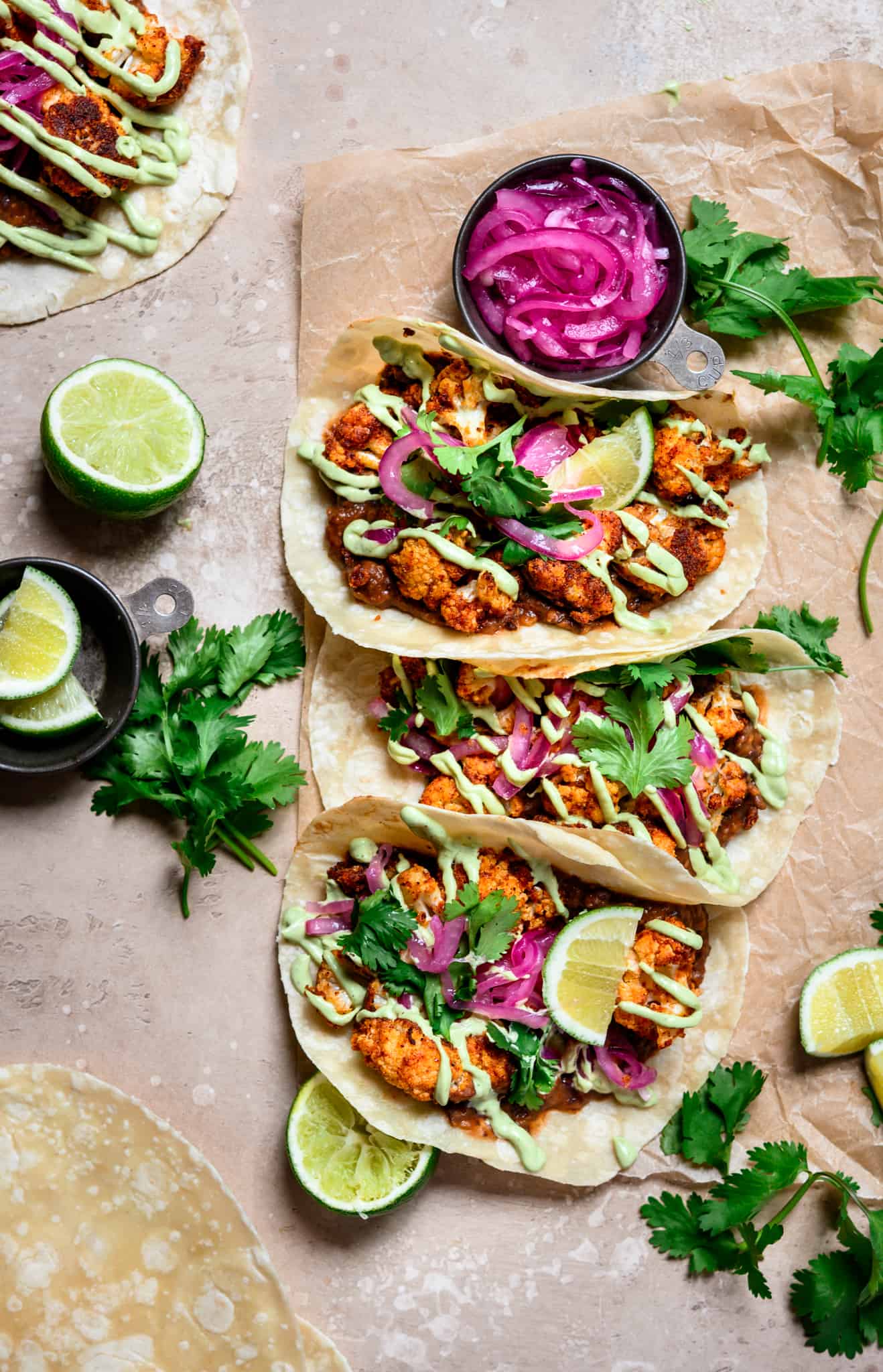 Overhead view of 3 spicy black bean and cauliflower tacos with pickled red onion on light brown background