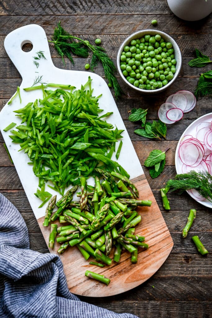 Overhead view of spring vegetables on a white cutting board