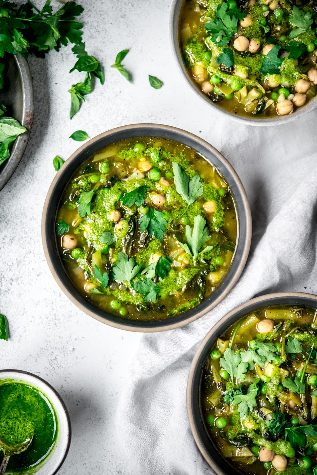 Overhead view of bowls of green vegetable soup on white background