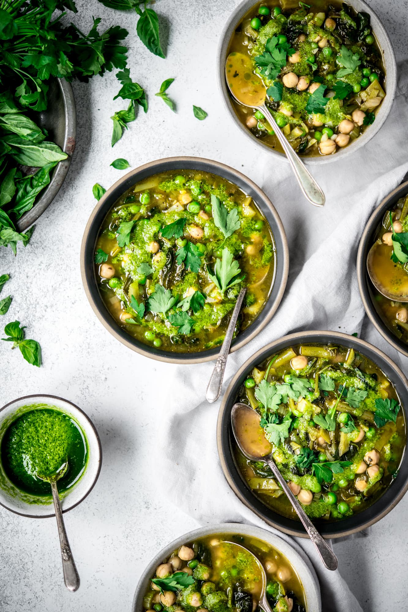 Overhead view of 5 bowls of super green vegetable soup with spoons on white background