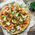 Overhead view of vegan buffalo cauliflower pizza with avocado slices and ranch drizzle on parchment paper