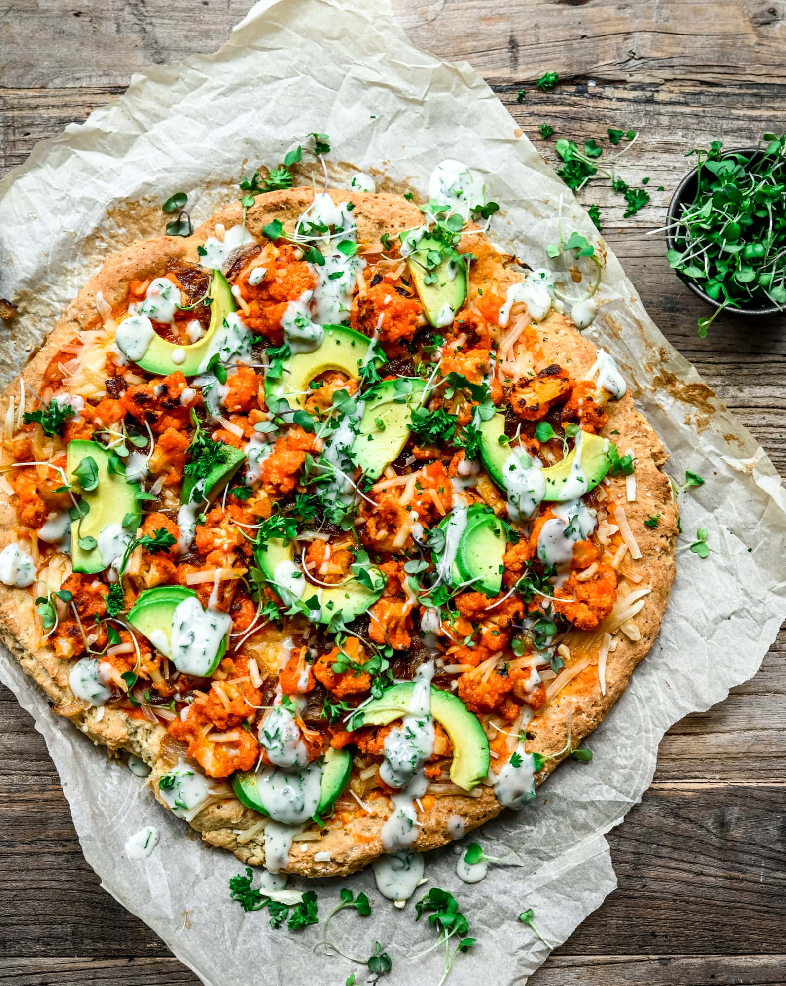 Overhead view of vegan comfort food pizza with avocado slices and ranch drizzle on parchment paper