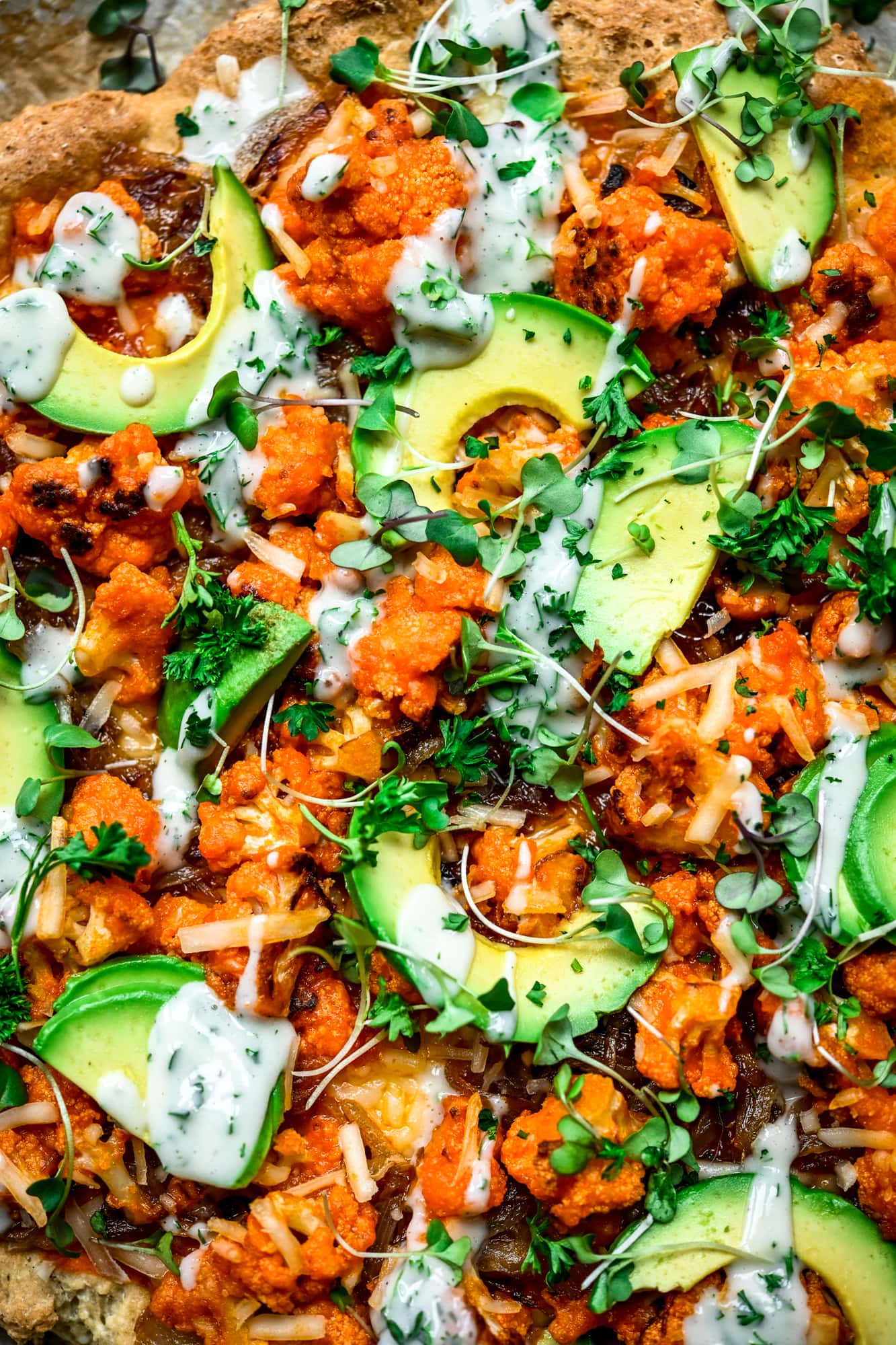 Overhead view of vegan buffalo cauliflower pizza with avocado slices and ranch drizzle on parchment paper
