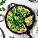 Overhead view of vegan spring vegetable frittata in a cast iron skillet on white background