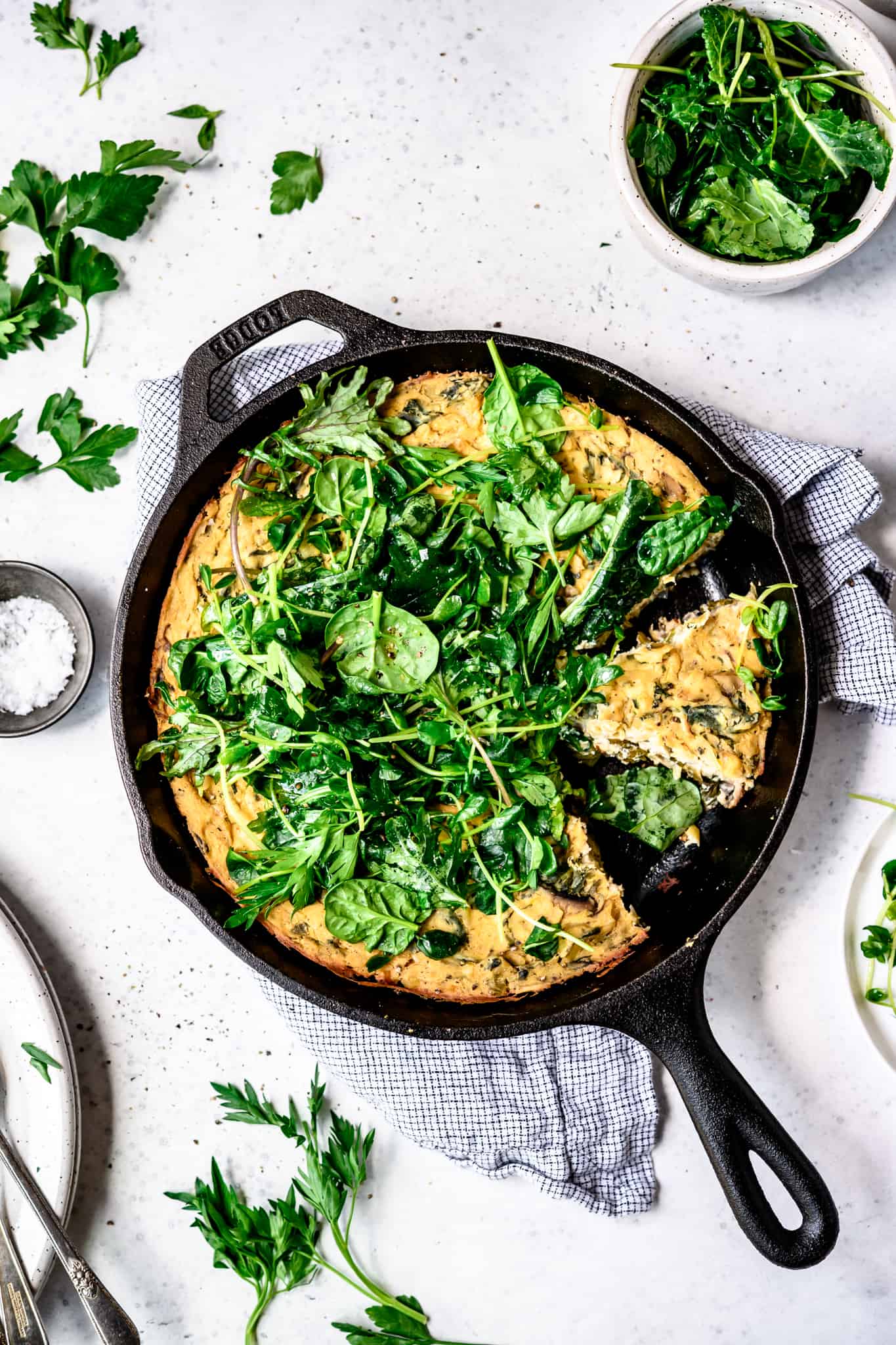 Overhead view of vegan spring vegetable frittata in a cast iron skillet on white background