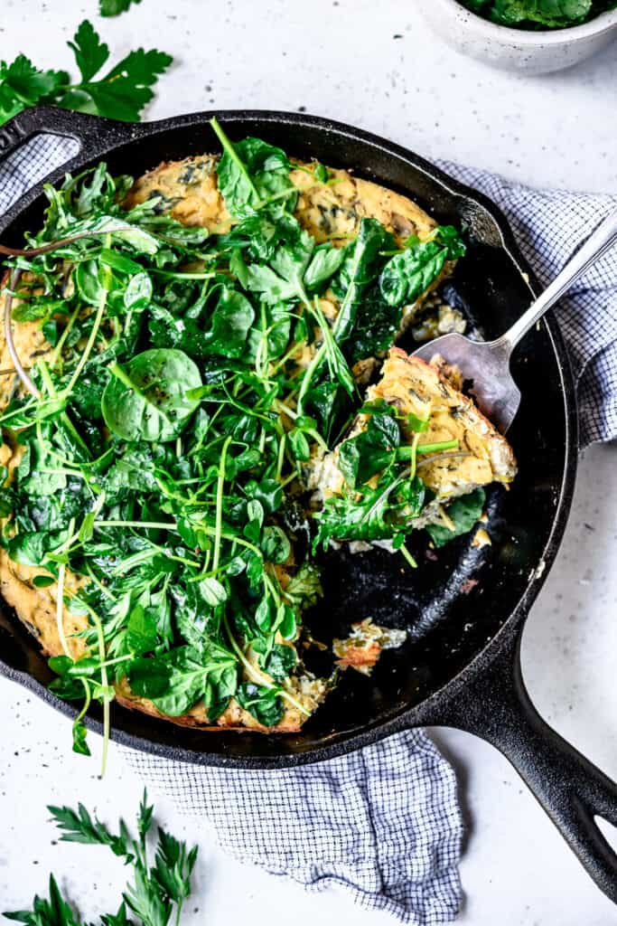 Overhead view of vegan spring vegetable frittata in a cast iron skillet on white background