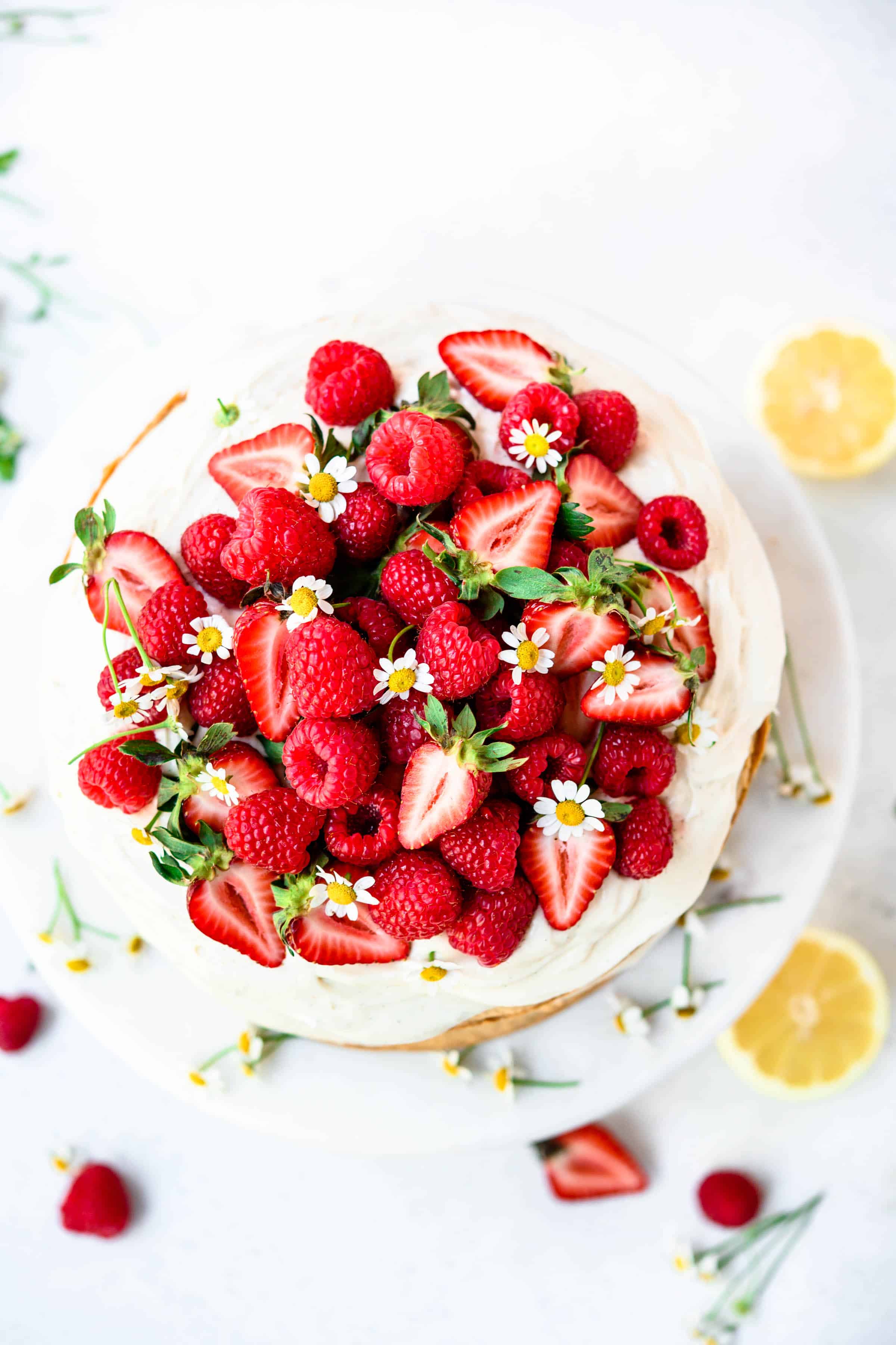 Overhead view of vanilla layer cake topped with fresh berries and flowers on marble cake stand