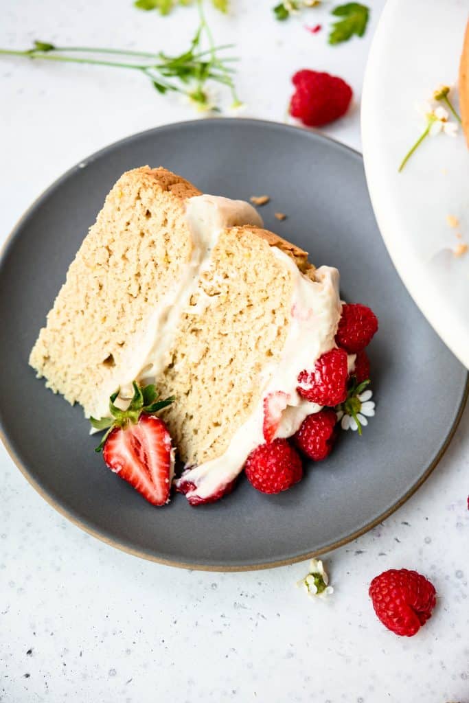 High side view of slice of vanilla layer cake topped with fresh berries on a gray plate