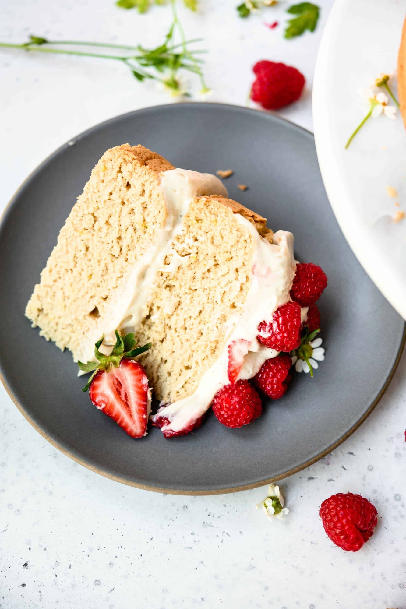 High side view of slice of vanilla layer cake topped with fresh berries on a gray plate