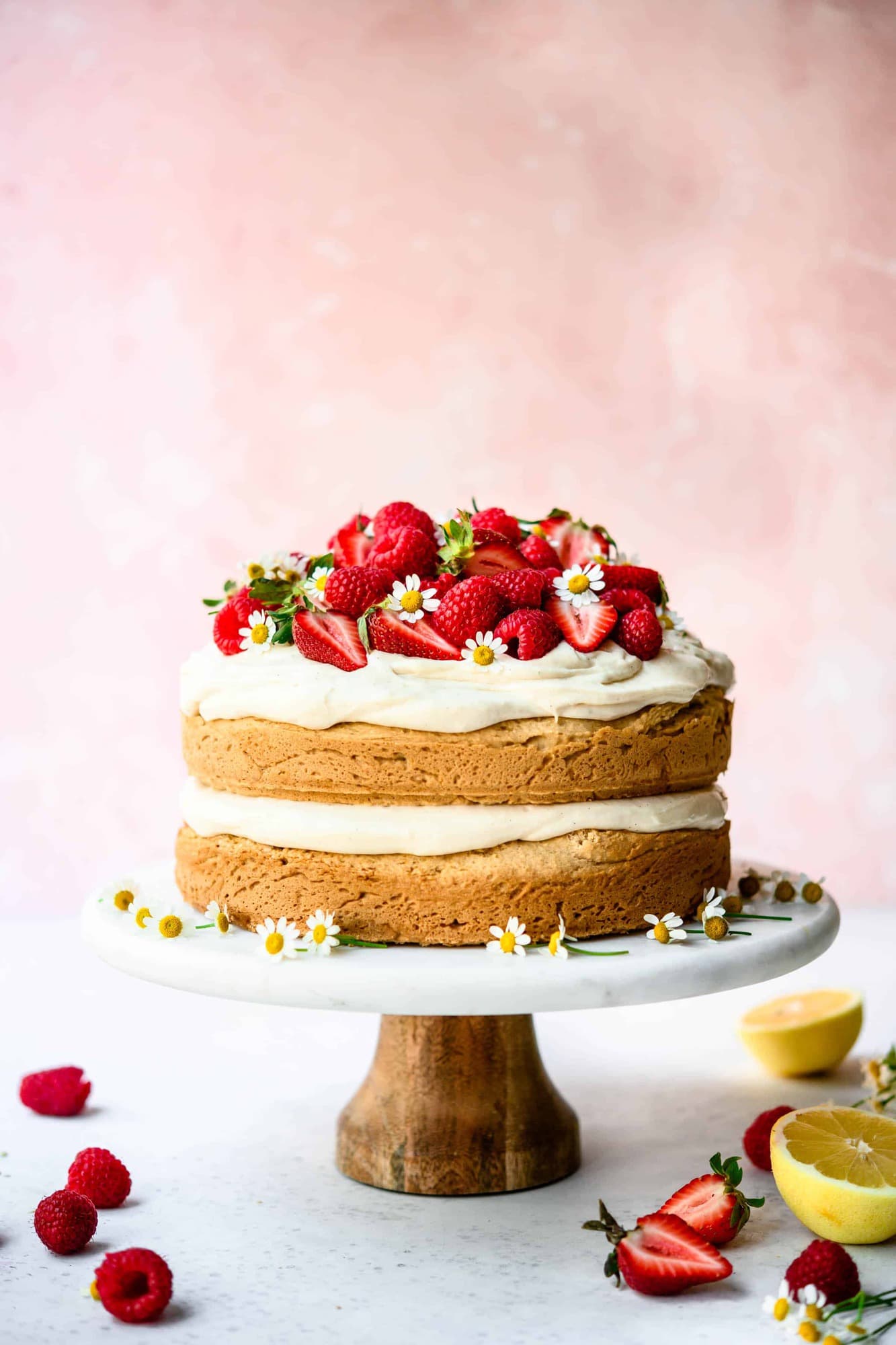 Side view of lemon almond layer cake topped with fresh berries on marble cake stand