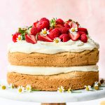 Side view of lemon almond layer cake topped with fresh berries on marble cake stand