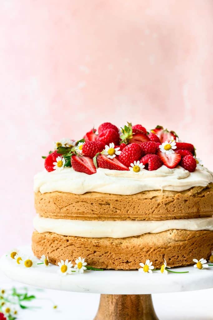 Side view of lemon almond layer cake topped with fresh berries on marble cake stand