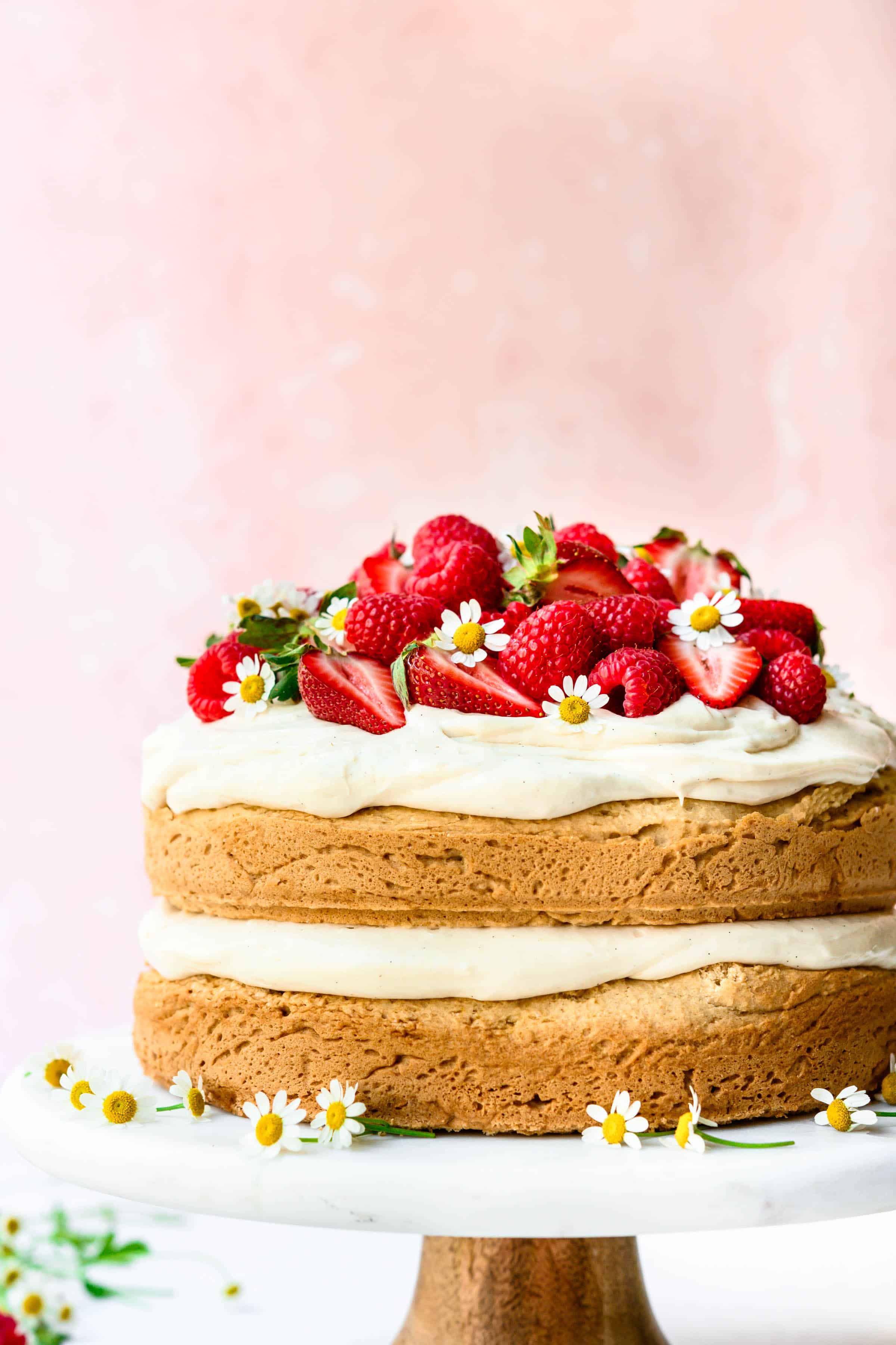 Side view of lemon almond layer cake topped with fresh berries on marble cake stand