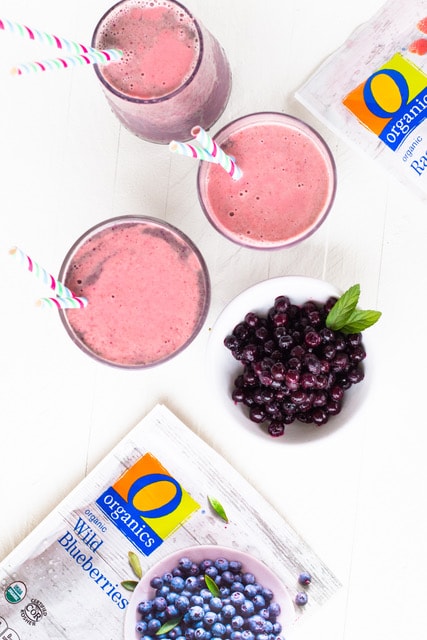 Overhead view of three blueberry smoothies next to a bowl of frozen blueberries