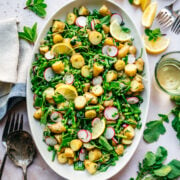 overhead view of asparagus potato salad with peas and radishes on a large white platter.