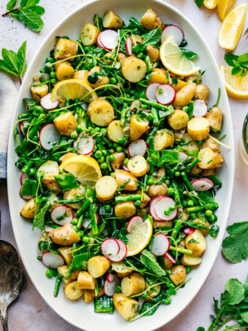 overhead view of asparagus potato salad with peas and radishes on a large white platter.