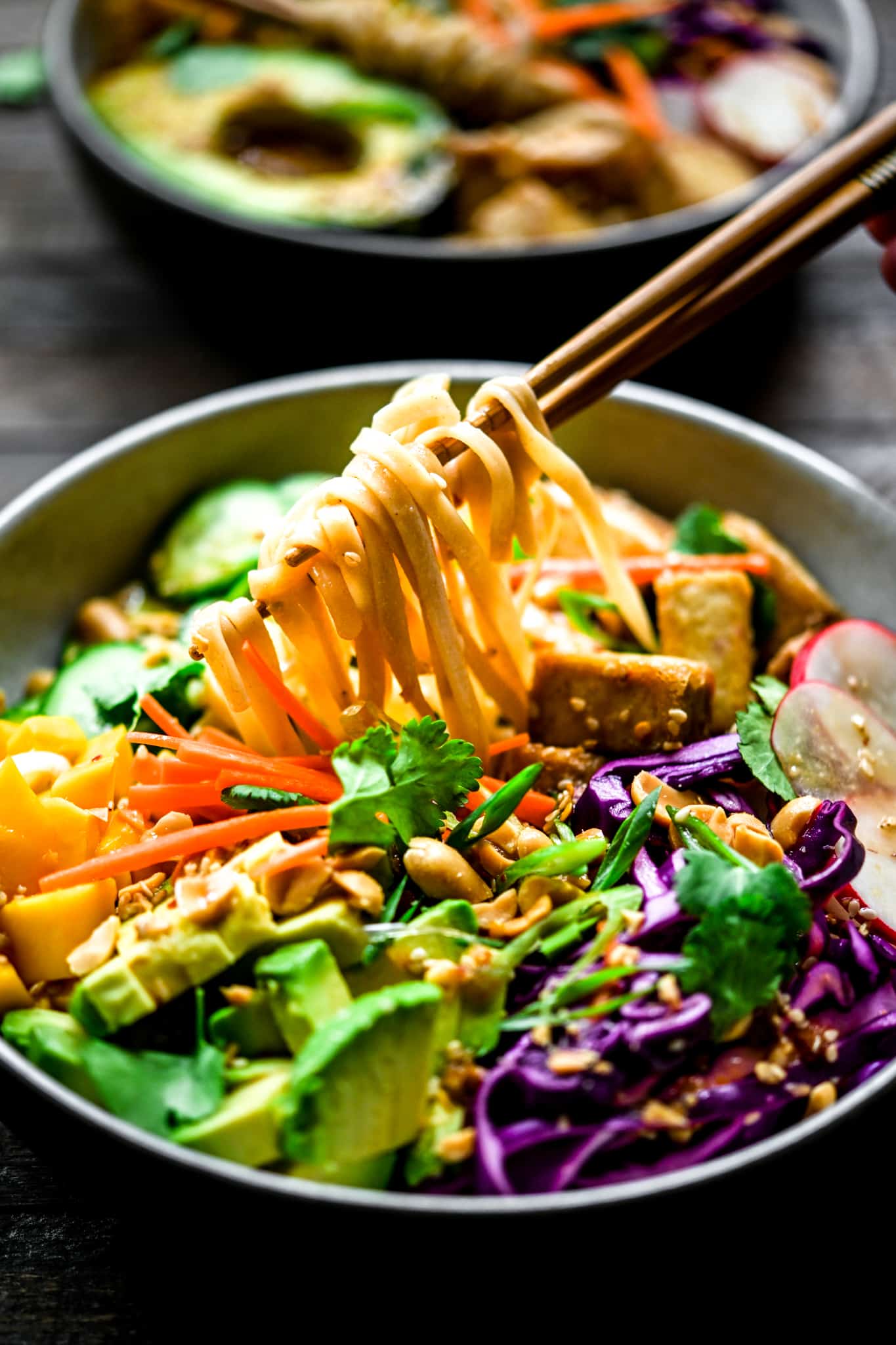 Side view of chopsticks picking up rice noodles from vegan spring roll bowls for meal prep