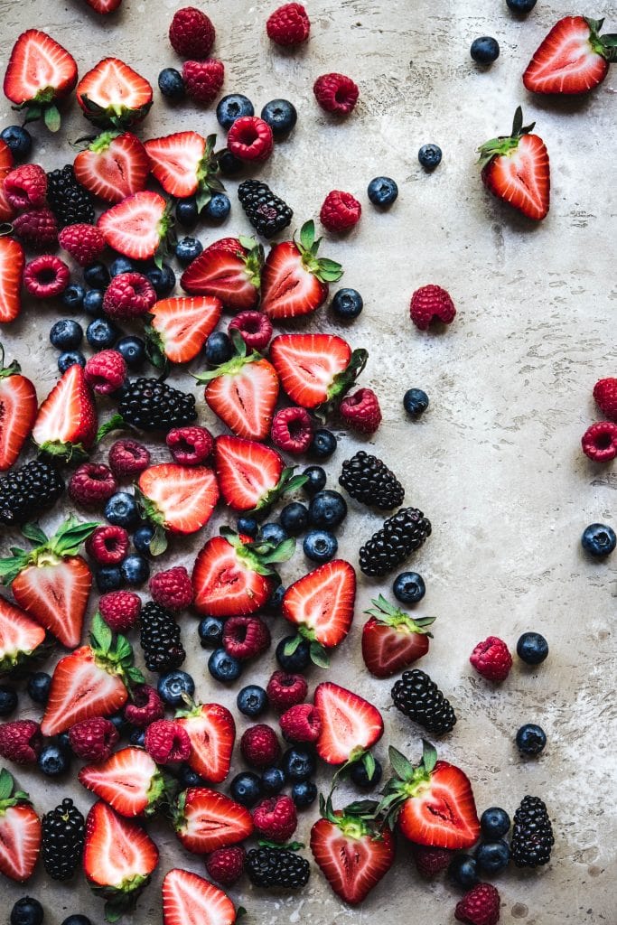 Overhead view of beautiful food photography of fresh blueberries, raspberries, strawberries and blackberries on rustic tan background
