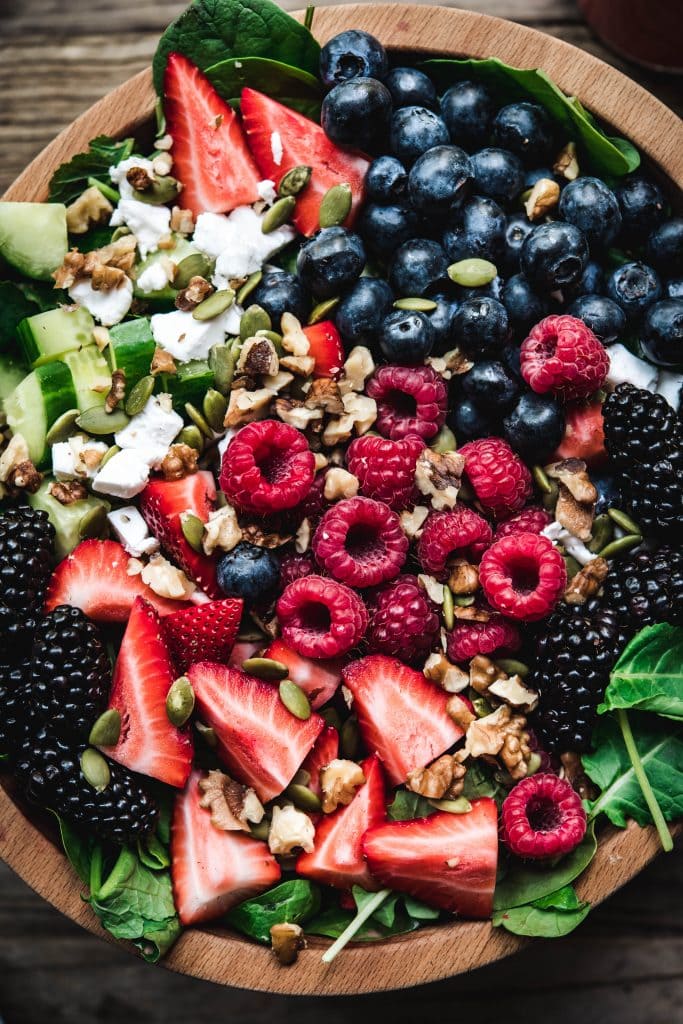 Close up Overhead view of berry spinach salad with feta and cucumbers in wooden bowl