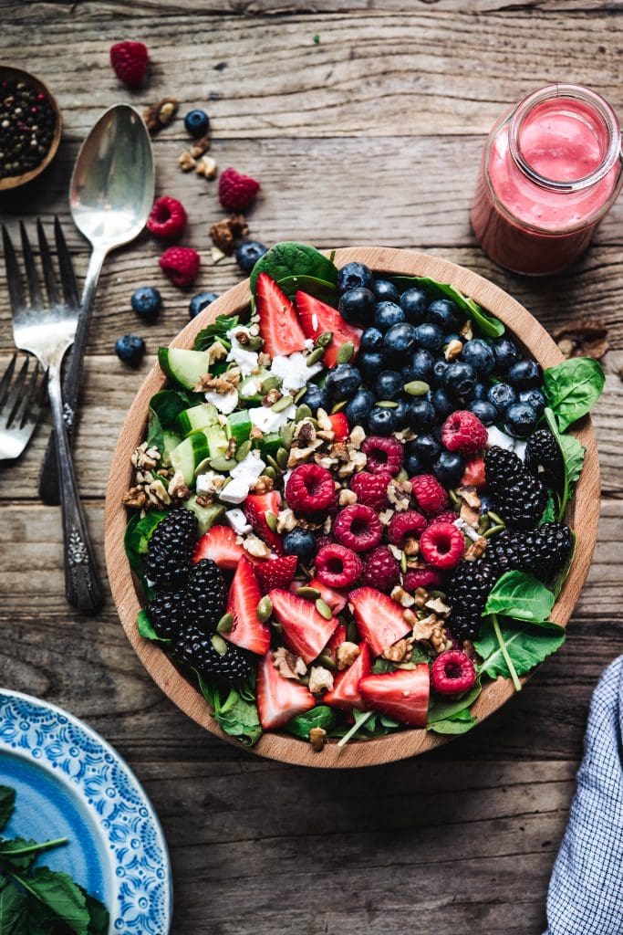 Overhead view of berry spinach salad with feta and cucumbers in wooden bowl