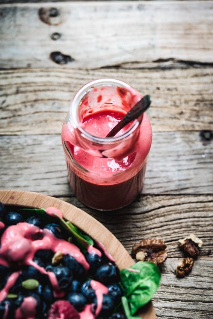 Close up overhead of vegan raspberry dressing in a small glass jar with spoon on wood table