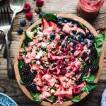 Overhead view of berry spinach salad with raspberry dressing and feta and cucumbers in wooden bowl