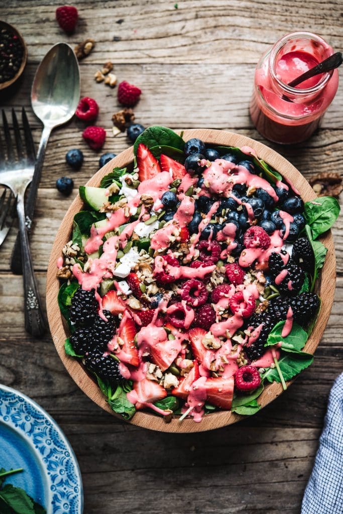 Overhead view of berry spinach salad with raspberry dressing and feta and cucumbers in wooden bowl