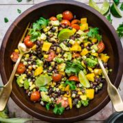 Black bean and mango salad in a wooden bowl with a fork and a spoon to toss.