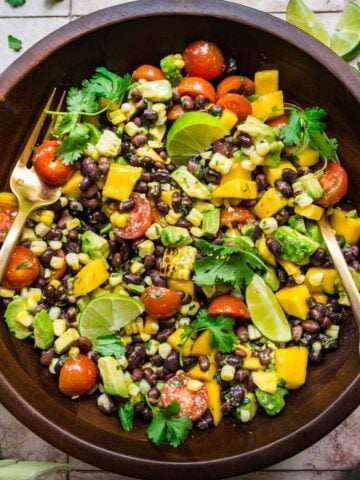 Black bean and mango salad in a wooden bowl with a fork and a spoon to toss.