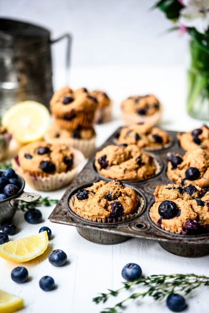 Side view of vegan blueberry lemon muffins in rustic muffin tin on white background