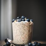 Side view of carrot cake overnight oats in a glass jar topped with blueberries on a stack of antique books