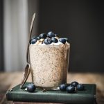 Side view of carrot cake overnight oats in a glass jar topped with blueberries on a stack of antique books