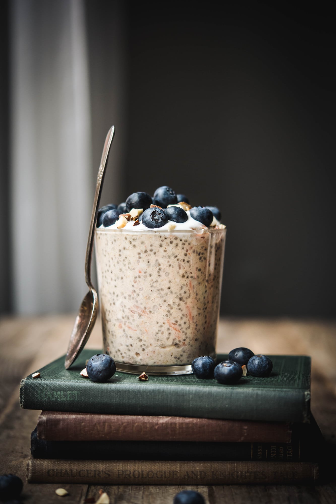 Side view of carrot cake overnight oats in a glass jar topped with blueberries on a stack of antique books