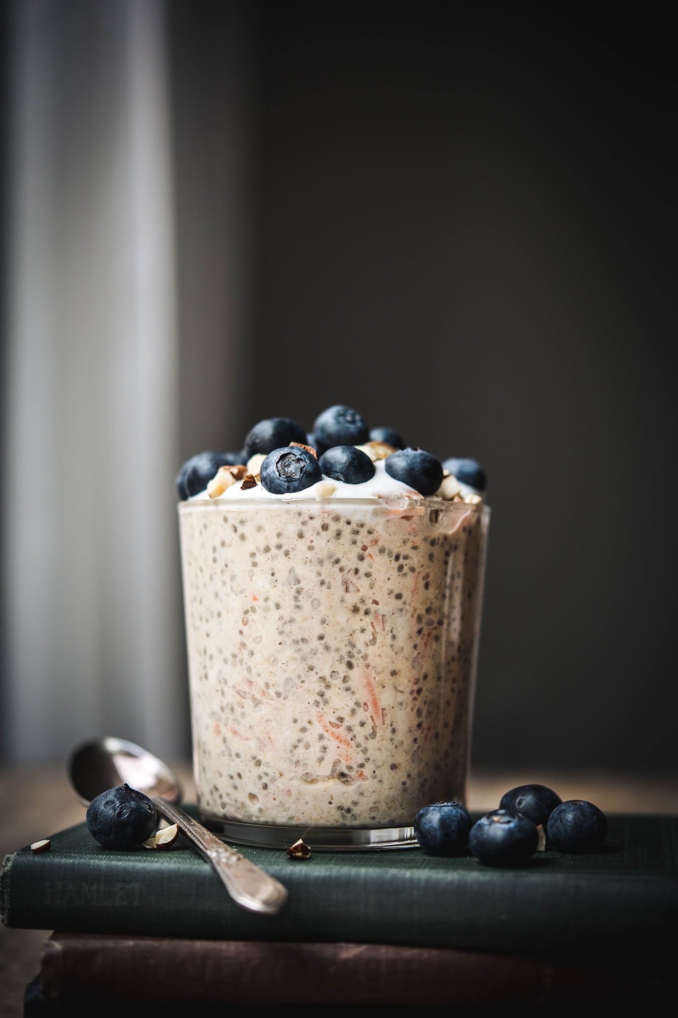 Side view of carrot cake overnight oats in a glass jar topped with blueberries on a stack of antique books