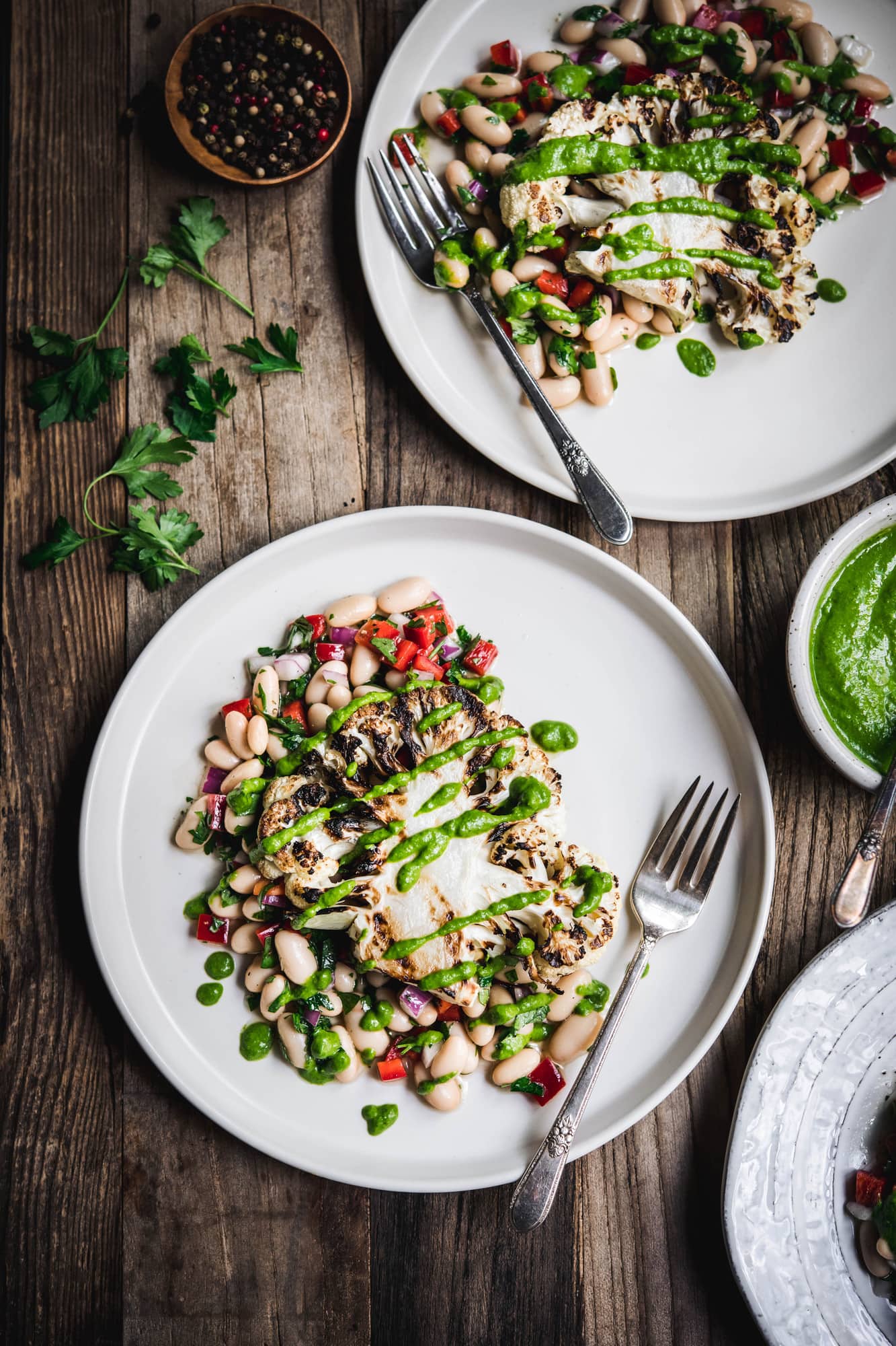 Overhead view of grilled cauliflower steaks over white bean salad on a white plate on wood table