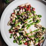 Close up Overhead view of grilled cauliflower steaks over white bean salad on a white plate on wood table