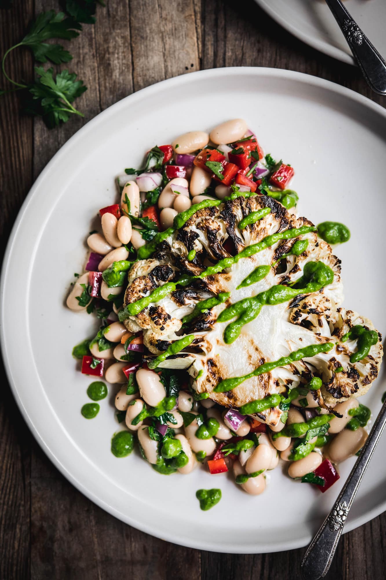 Close up Overhead view of grilled cauliflower steaks over white bean salad on a white plate on wood table