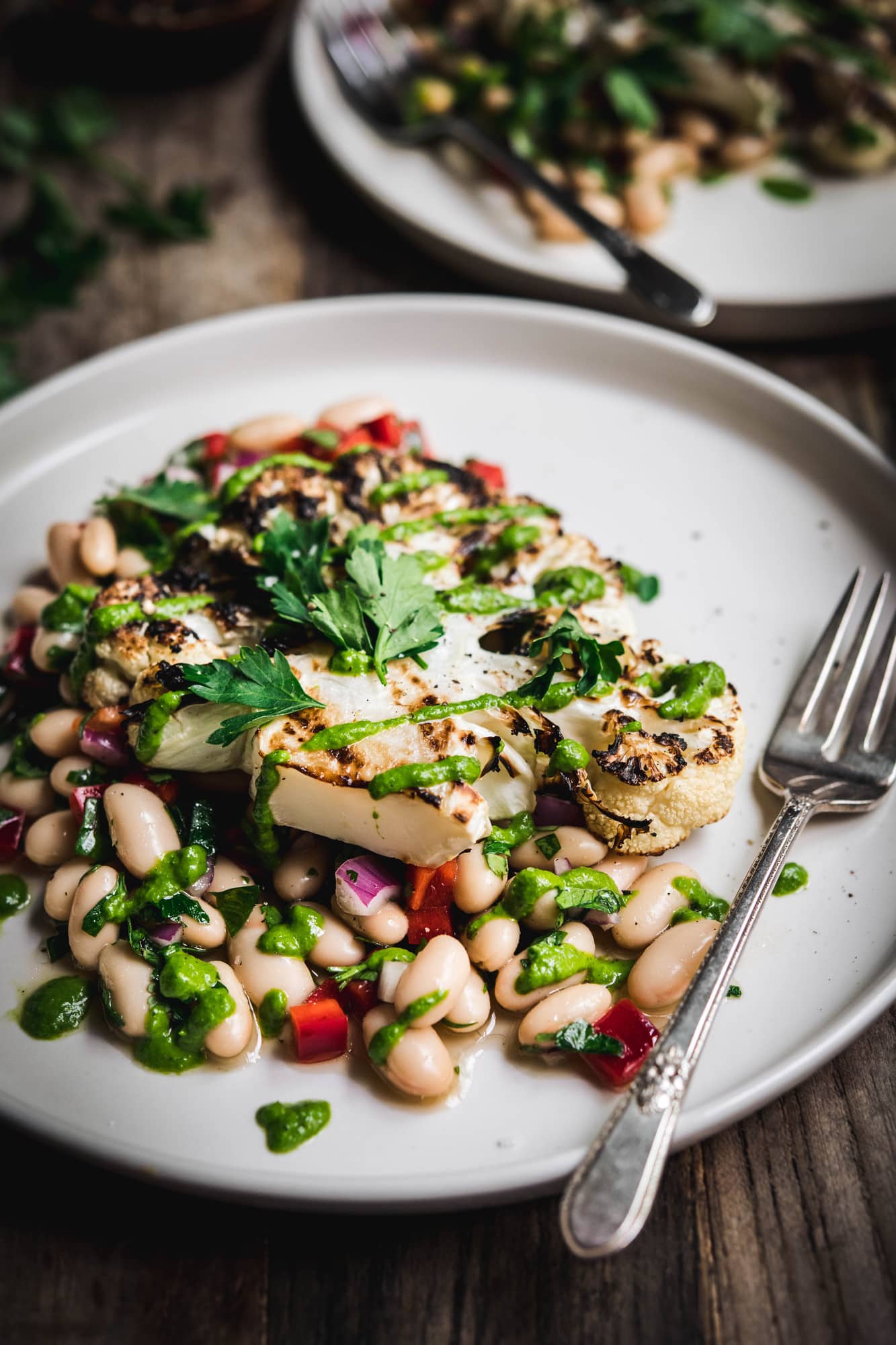 Side view of grilled cauliflower steaks over white bean salad on a white plate on wood table