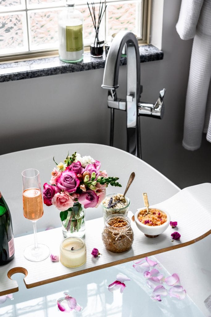 Side view of relaxing bath tub with body scrubs, champagne, flowers and candles