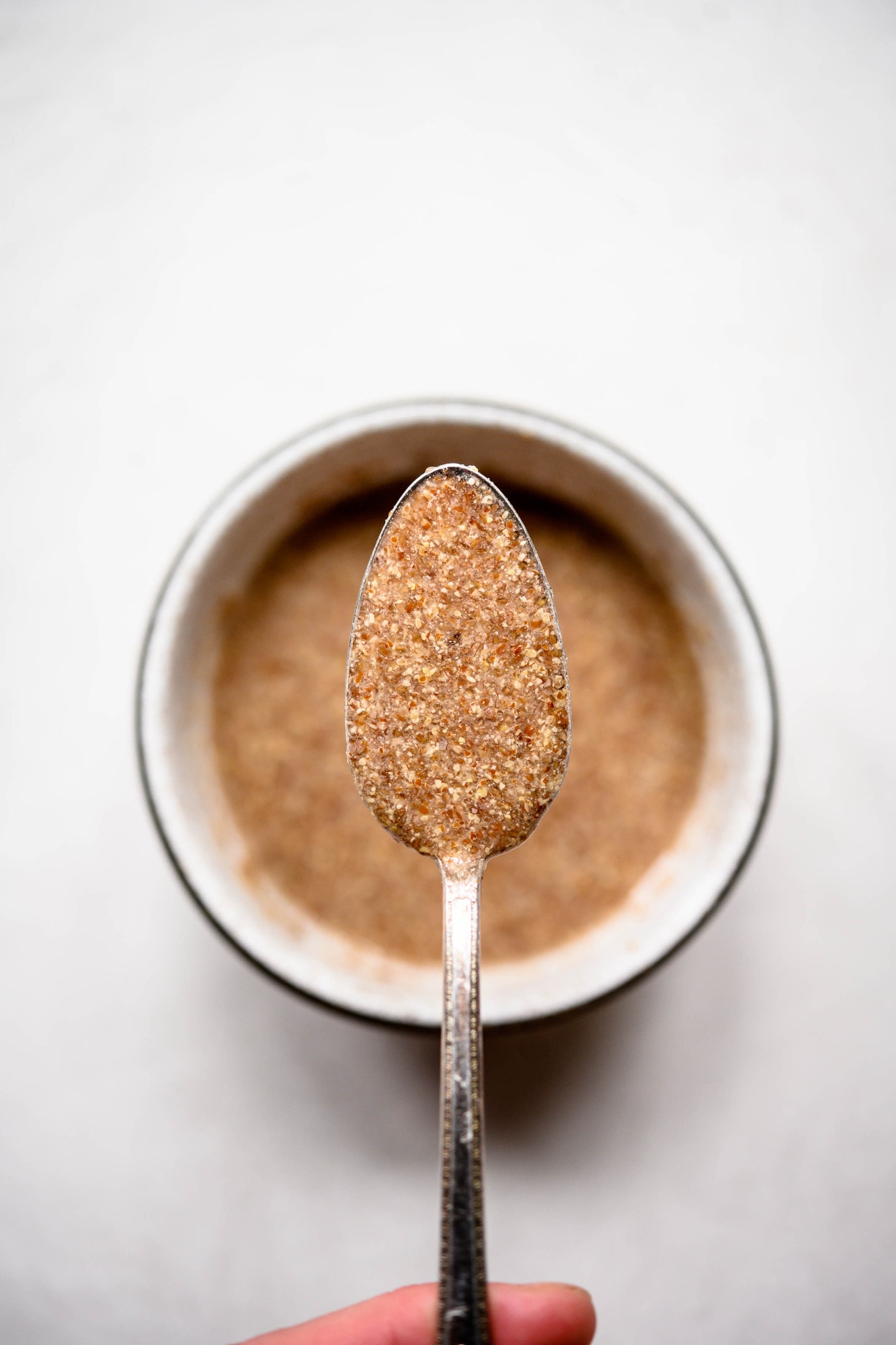 Close up of person holding spoon of flax egg over bowl on white background