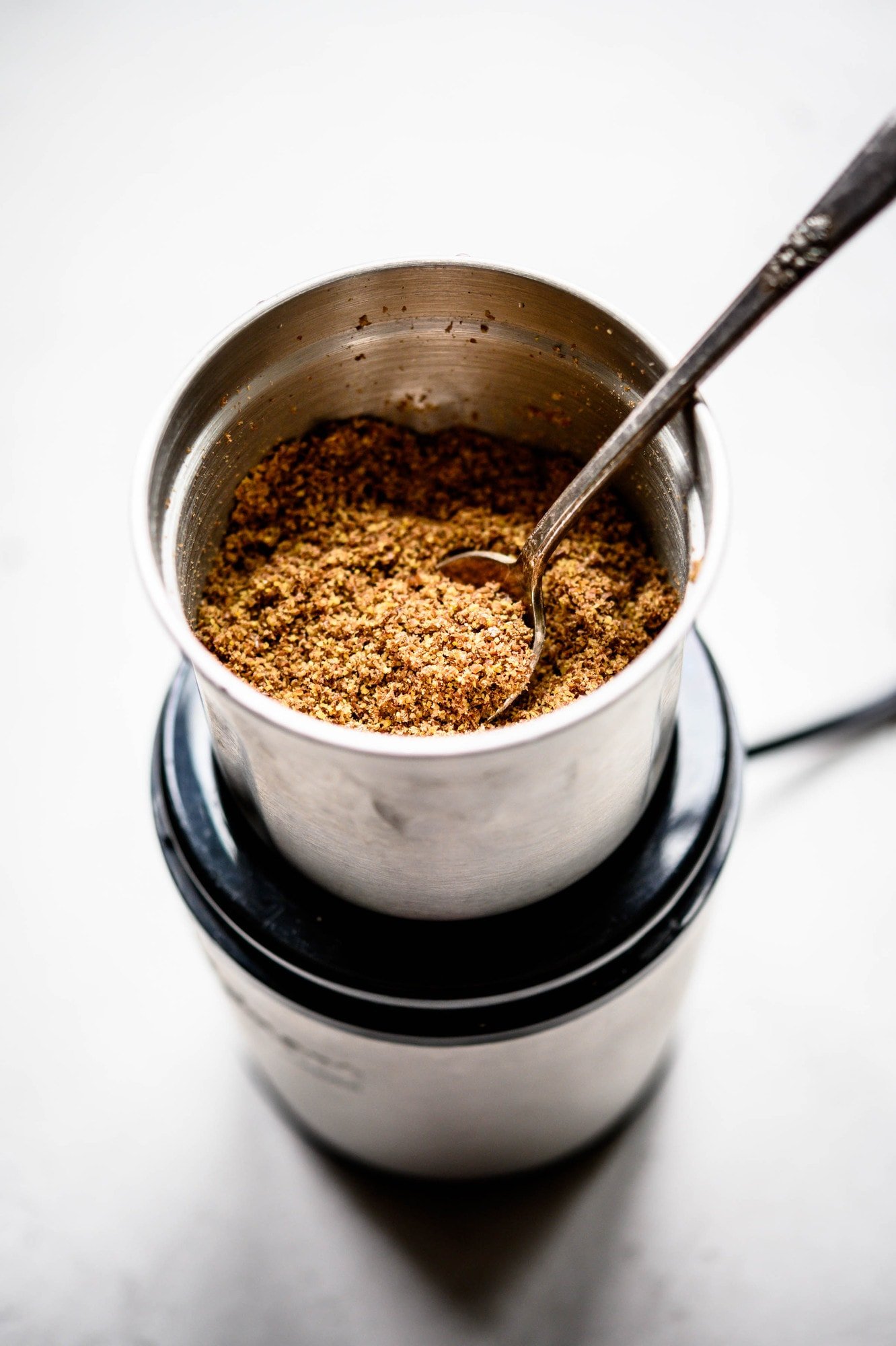 Side view of flax meal in spice grinder with spoon