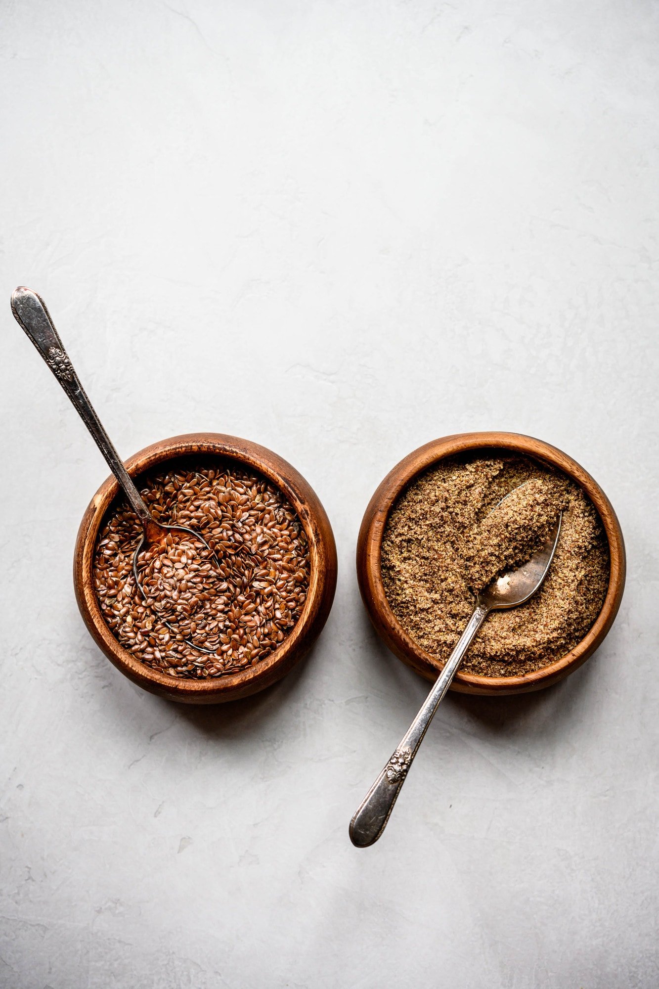 Overhead flax seed and flax meal in two small wooden bowls on white background