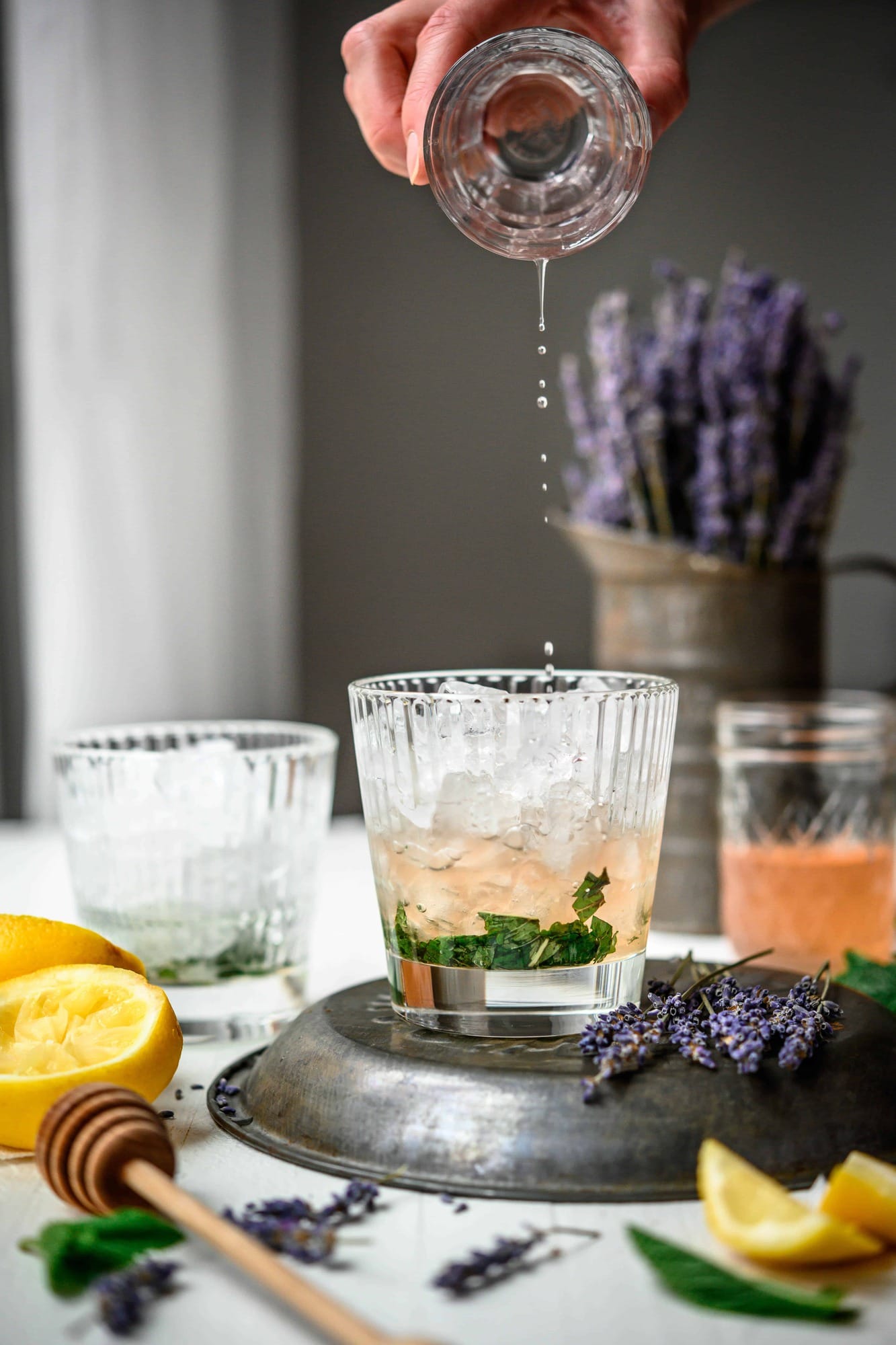 Side view of pouring homemade lemon lavender simple syrup over ice and muddled mint