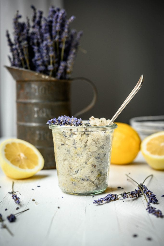 Side view of lavender lemon sugar scrub in glass jar with dried lavender and lemons in background